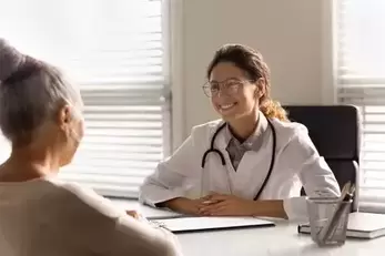 Smiling young female doctor talk consult mature patient at consultation in private clinic. 