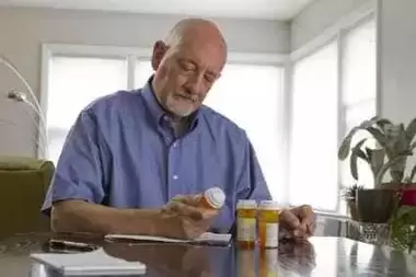 Elderly man at table looking at prescription bottles