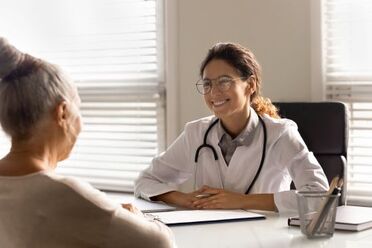 Picture of older female patient sitting at young female doctor's desk talking and laughing